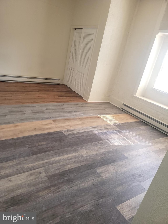 unfurnished bedroom with a closet, a baseboard radiator, and wood finished floors