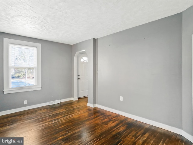 spare room with dark wood-type flooring, visible vents, a textured ceiling, and baseboards