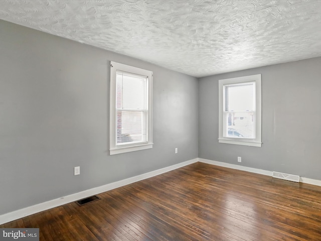 spare room featuring baseboards, visible vents, a textured ceiling, and hardwood / wood-style floors