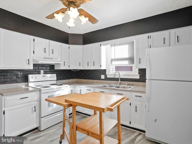 kitchen with white appliances, white cabinets, light countertops, under cabinet range hood, and a sink