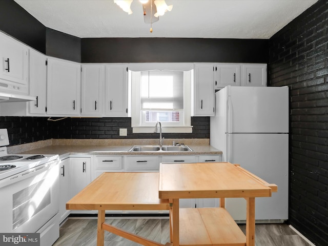 kitchen featuring white appliances, white cabinetry, a sink, and under cabinet range hood