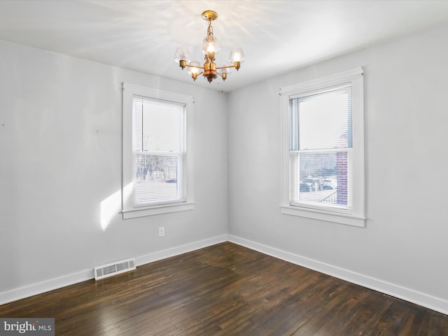 empty room with a notable chandelier, dark wood-type flooring, visible vents, and a healthy amount of sunlight