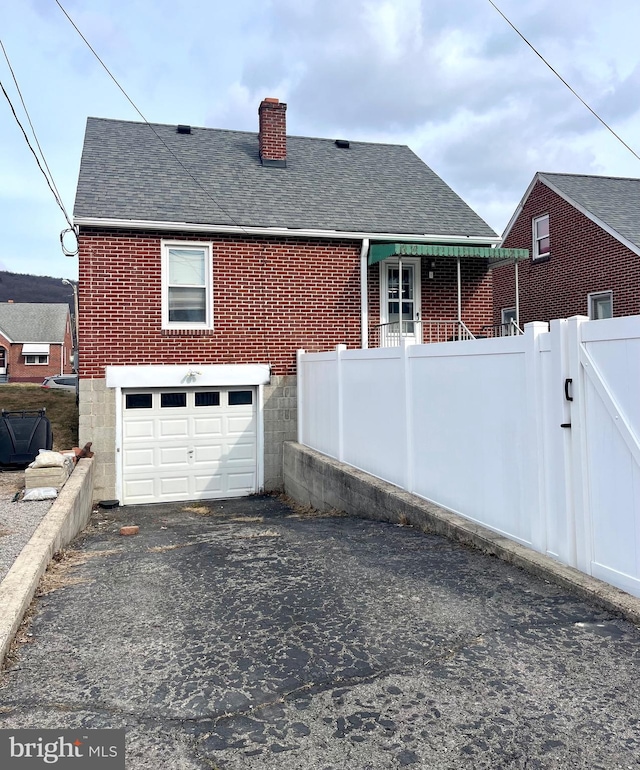 back of property featuring a chimney, aphalt driveway, roof with shingles, fence, and brick siding