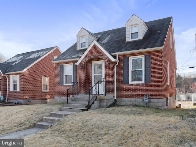 new england style home with brick siding, a shingled roof, and a front yard