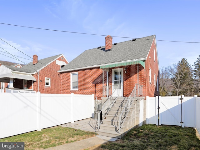 rear view of property featuring a fenced backyard, a gate, a shingled roof, and brick siding