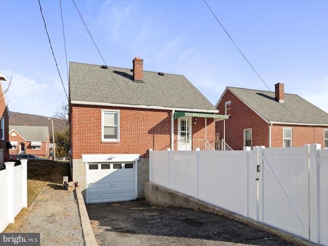 back of property with brick siding, fence, roof with shingles, a gate, and a chimney