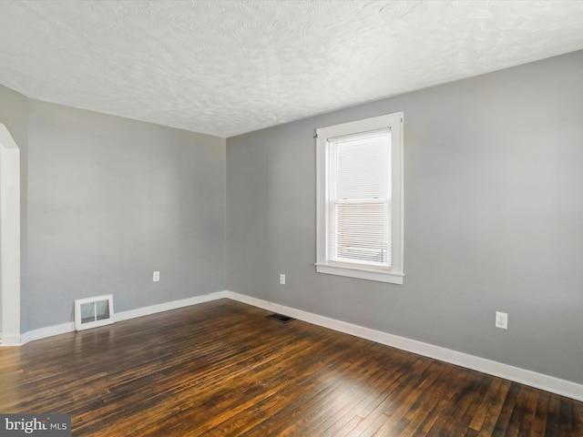 empty room with dark wood-type flooring, visible vents, a textured ceiling, and baseboards