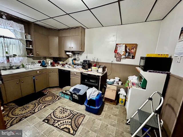 kitchen featuring black dishwasher, a wainscoted wall, a paneled ceiling, light countertops, and a sink