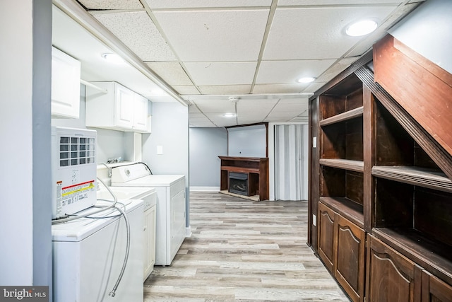 clothes washing area featuring cabinet space, a fireplace, light wood finished floors, and washing machine and clothes dryer