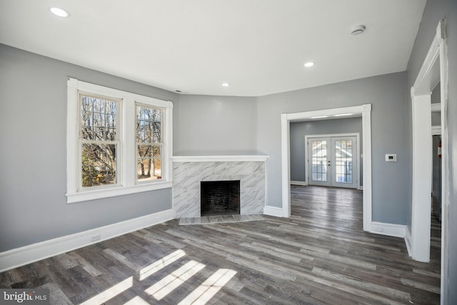 unfurnished living room with a premium fireplace, baseboards, dark wood finished floors, and french doors