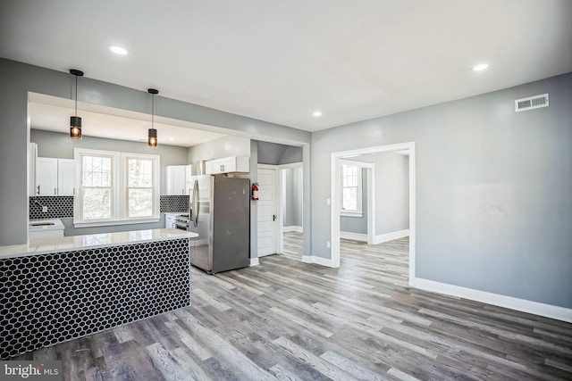 kitchen with light countertops, visible vents, backsplash, freestanding refrigerator, and white cabinetry