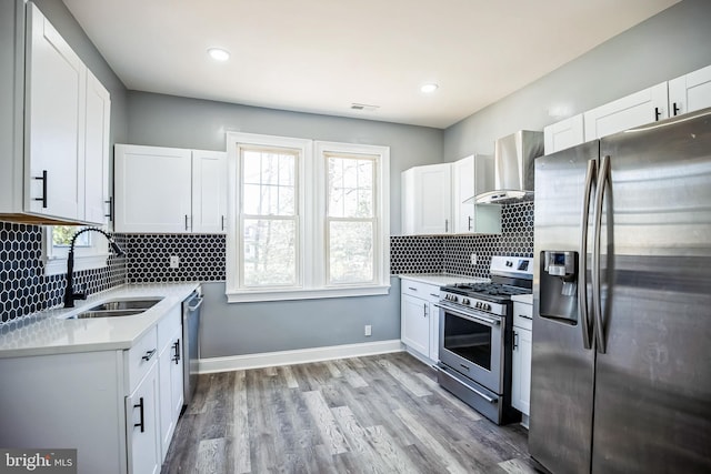 kitchen featuring appliances with stainless steel finishes, light countertops, wall chimney range hood, and white cabinetry