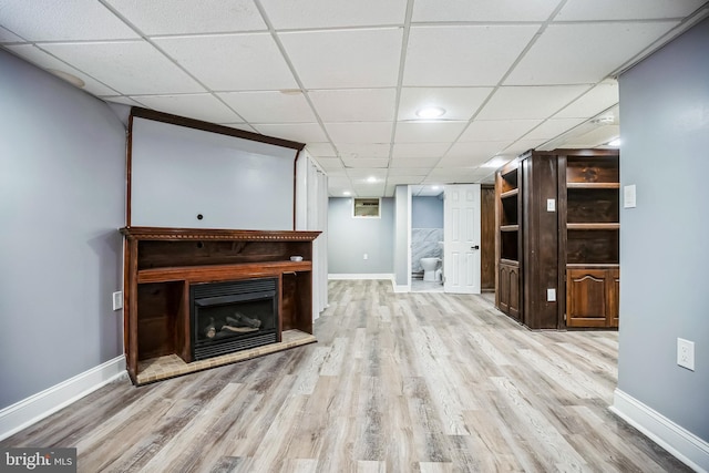 living room with light wood-style flooring, baseboards, a fireplace with raised hearth, and a drop ceiling