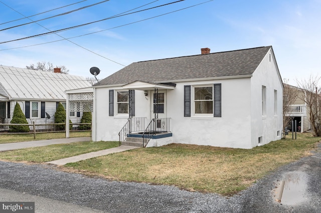 bungalow-style home featuring a front yard, roof with shingles, a chimney, and stucco siding