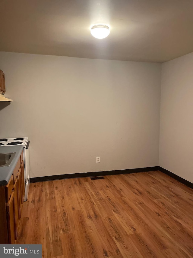 kitchen featuring under cabinet range hood, visible vents, baseboards, light wood-type flooring, and brown cabinetry