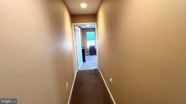 corridor with baseboards and dark carpet