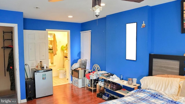 bedroom with ensuite bathroom, fridge, wood finished floors, and recessed lighting