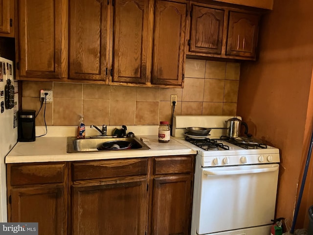 kitchen featuring light countertops, backsplash, a sink, and white range with gas cooktop