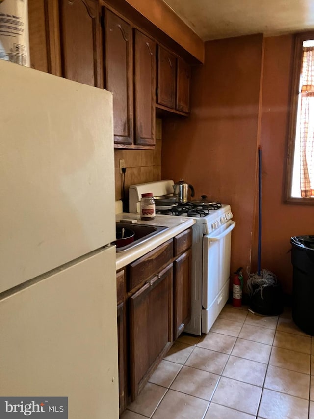 kitchen featuring white appliances, light tile patterned floors, backsplash, light countertops, and a sink