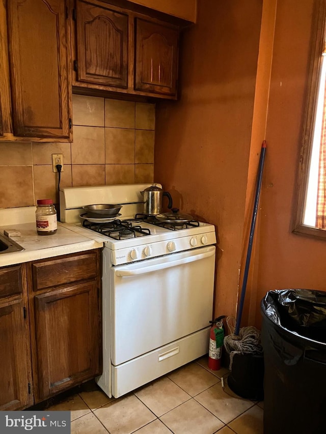 kitchen with light tile patterned floors, light countertops, tasteful backsplash, and white range with gas stovetop