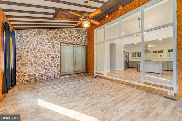 empty room with beam ceiling, visible vents, a high ceiling, wood finished floors, and ceiling fan with notable chandelier