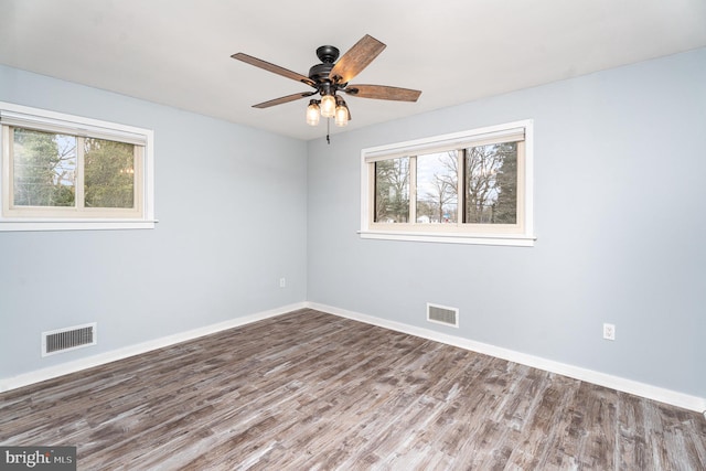 spare room with wood finished floors, visible vents, and baseboards