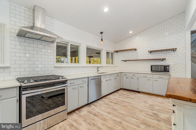 kitchen with stainless steel appliances, decorative backsplash, vaulted ceiling, a sink, and wall chimney range hood