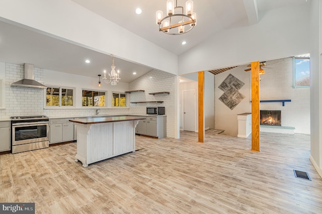 kitchen with light wood finished floors, plenty of natural light, wall chimney exhaust hood, appliances with stainless steel finishes, and a fireplace