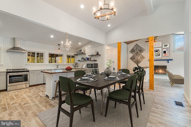 dining area featuring a chandelier, lofted ceiling, light wood-style floors, and a fireplace