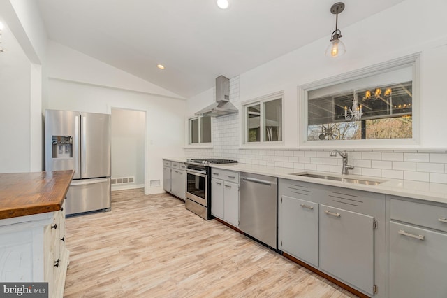 kitchen featuring stainless steel appliances, gray cabinets, wall chimney exhaust hood, and a sink