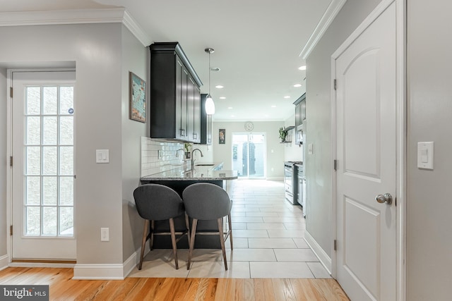 kitchen featuring light wood finished floors, baseboards, crown molding, stone counters, and backsplash