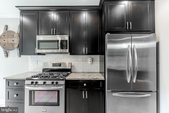 kitchen with light stone countertops, appliances with stainless steel finishes, decorative backsplash, and dark cabinets