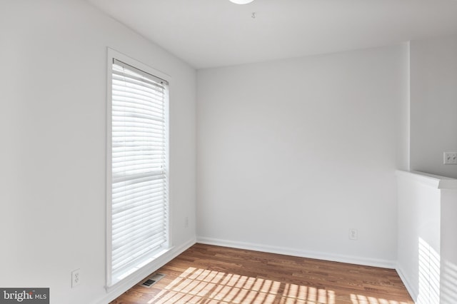 empty room featuring wood finished floors, visible vents, and baseboards