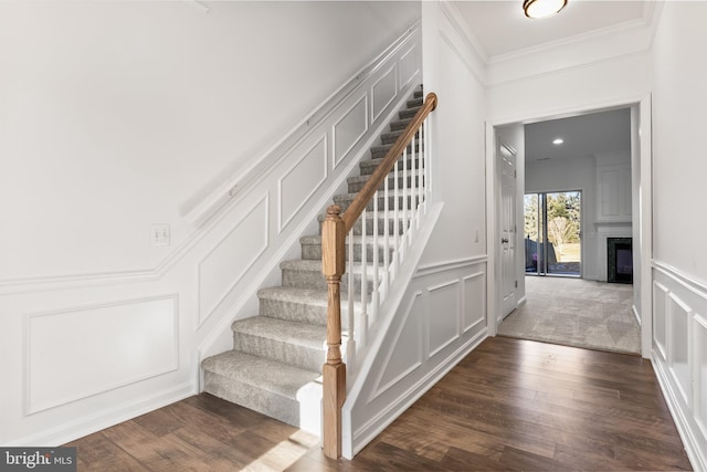 staircase with a fireplace, a decorative wall, crown molding, and wood finished floors