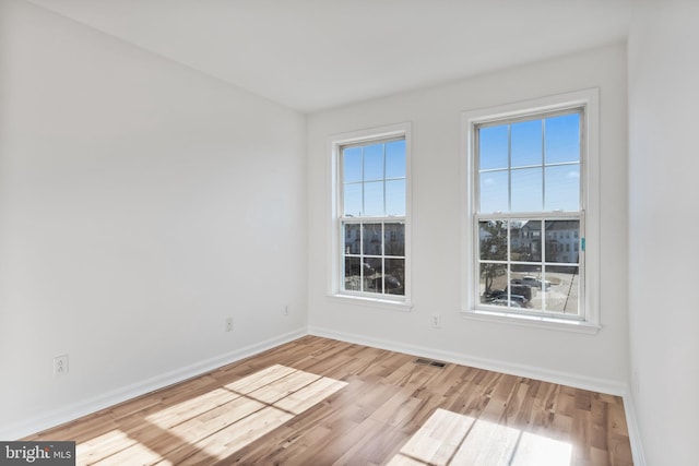 spare room with light wood finished floors, visible vents, and baseboards