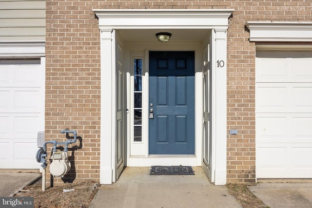 view of exterior entry featuring a garage and brick siding