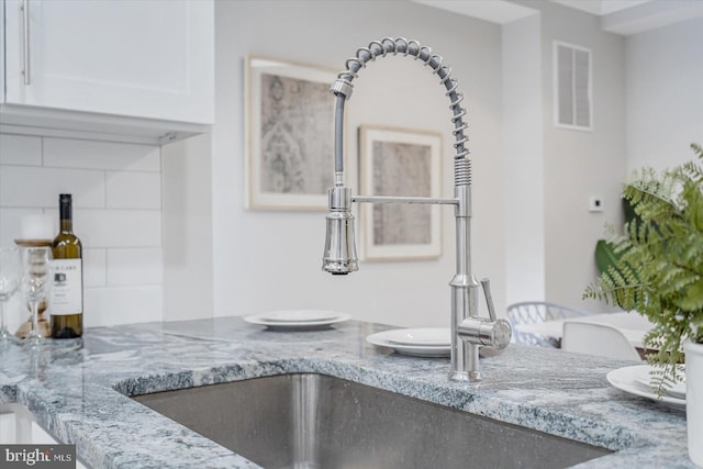 room details with white cabinets, visible vents, a sink, and light stone countertops