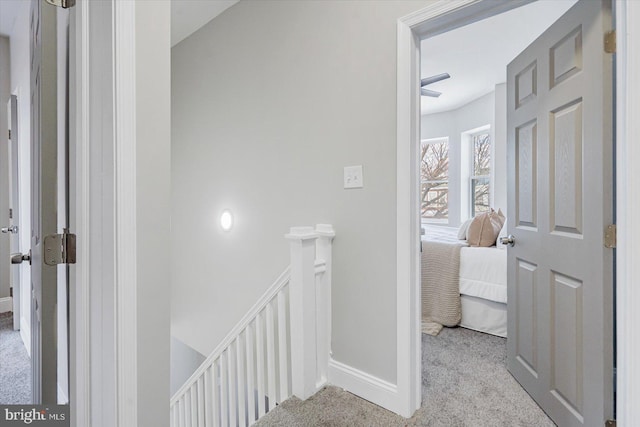 hallway featuring baseboards, light colored carpet, and an upstairs landing