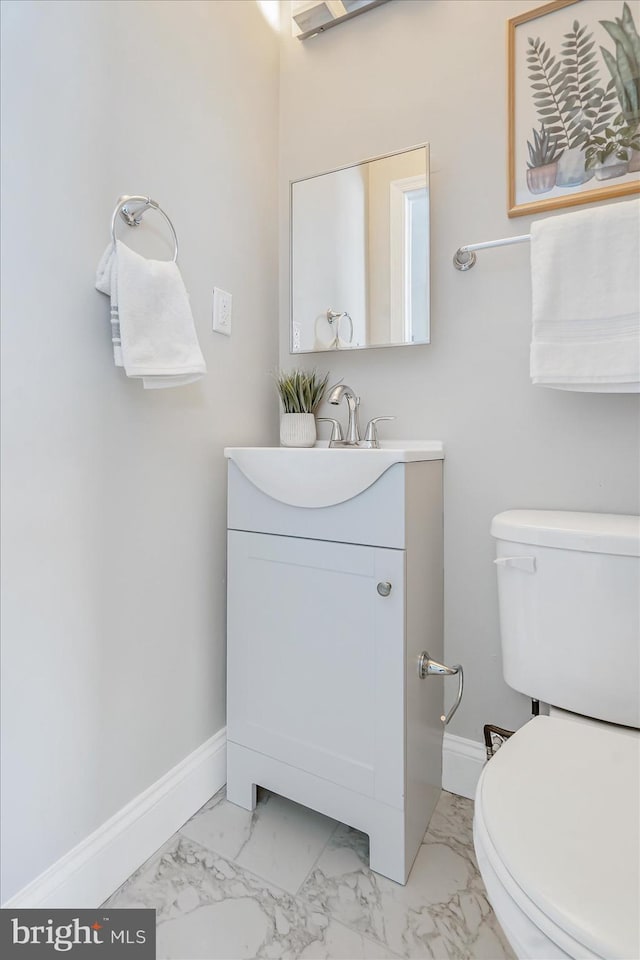 half bath featuring marble finish floor, baseboards, vanity, and toilet