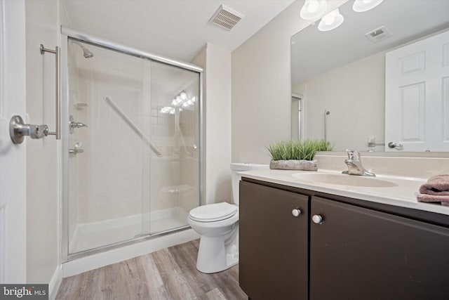 bathroom featuring visible vents, toilet, wood finished floors, vanity, and a shower stall