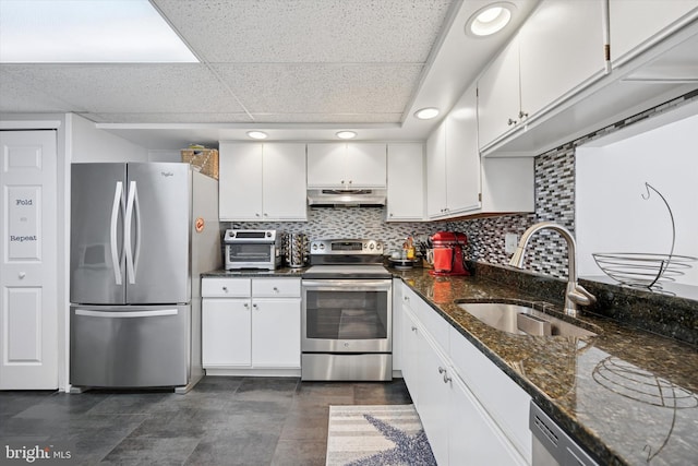 kitchen with decorative backsplash, appliances with stainless steel finishes, white cabinetry, a sink, and under cabinet range hood