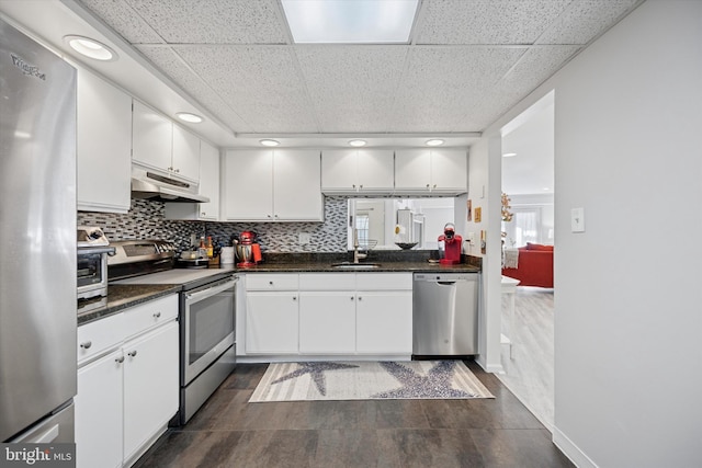 kitchen with white cabinets, dark countertops, stainless steel appliances, under cabinet range hood, and a sink