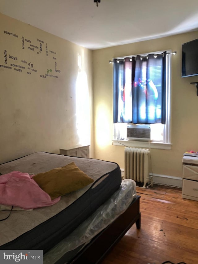 bedroom featuring cooling unit, radiator, and wood finished floors