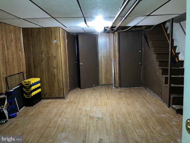 finished below grade area with a paneled ceiling, stairs, wooden walls, and wood finished floors