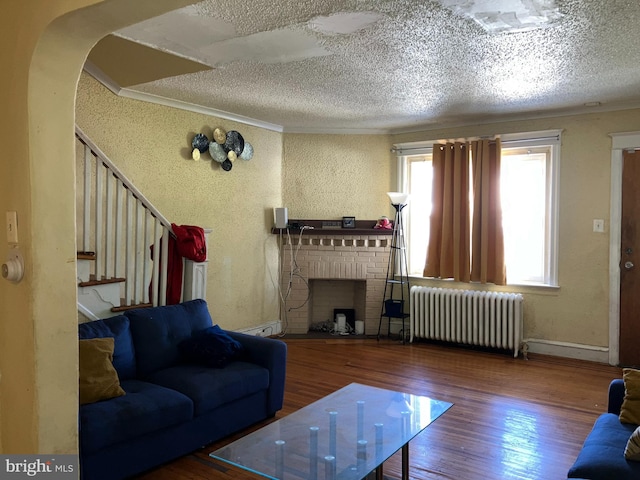 living area featuring a textured ceiling, wood finished floors, ornamental molding, a brick fireplace, and radiator