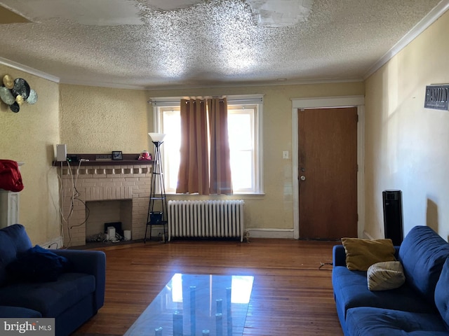 living area with a textured ceiling, wood finished floors, a brick fireplace, radiator, and crown molding