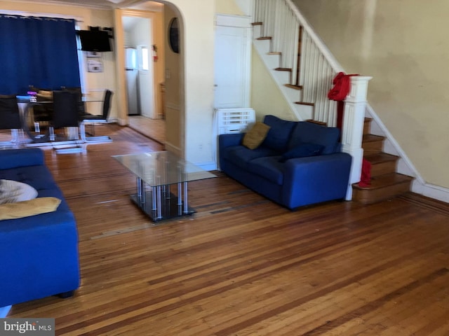 living area featuring stairs, arched walkways, baseboards, and wood finished floors