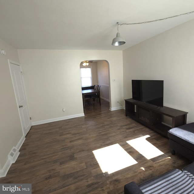 living room featuring arched walkways, wood finished floors, and baseboards