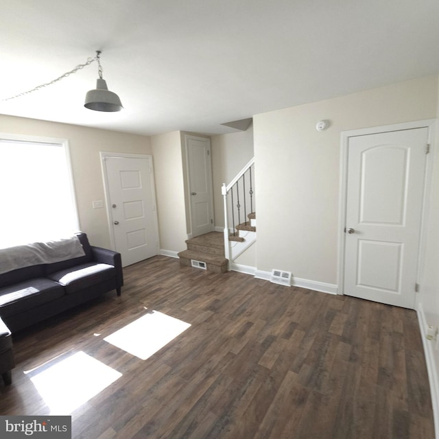 unfurnished living room featuring baseboards, visible vents, stairway, and dark wood-style flooring