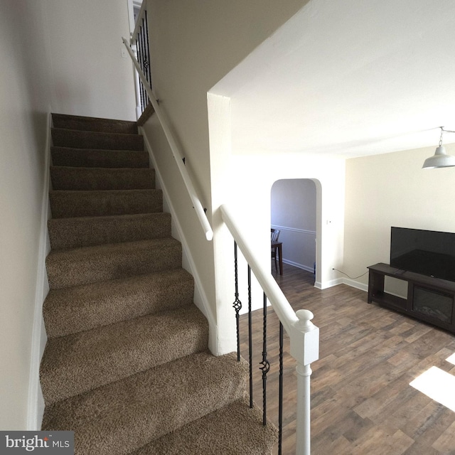 stairs with arched walkways, baseboards, and wood finished floors